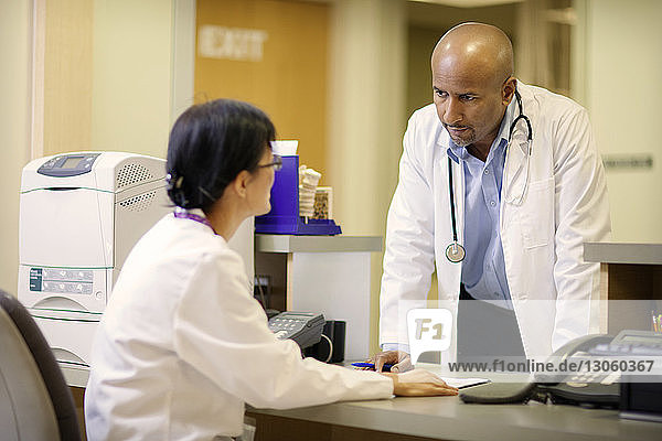 Männlicher Arzt bespricht sich mit weiblicher Ärztin am Schreibtisch im Krankenhaus