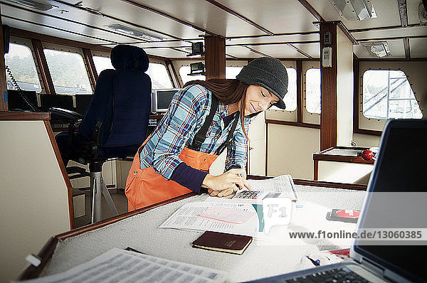 Frau benutzt Taschenrechner und schreibt auf Dokumente im Fischerboot
