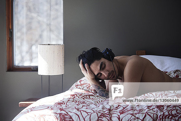 Mann ohne Hemd mit der Hand im Haar  der im Bett liegend Musik hört