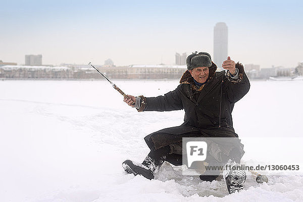 Glücklicher Mann beim Eisfischen im zugefrorenen See