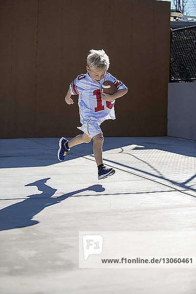 Boy running with football on sunny day