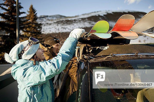 Seitenansicht einer Frau  die Skier aus dem Auto nimmt  während sie bei einem Freund im Skigebiet steht