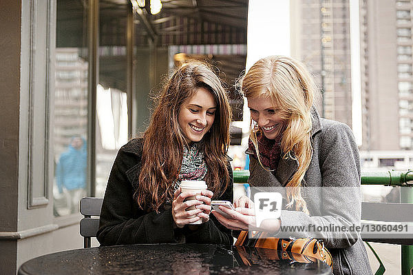 Glückliche Freunde telefonieren  während sie im Straßencafé sitzen