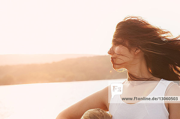 Frau mit zerzaustem Haar bei Sonnenuntergang gegen See
