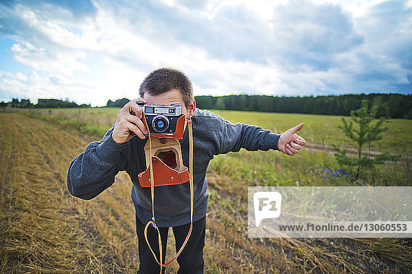 Man photographing while standing on grassy field against sky