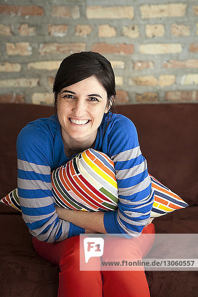 Portrait of happy young woman holding cushion while sitting on sofa