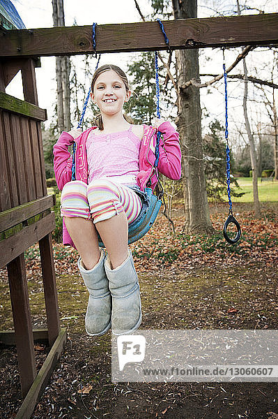 Portrait of smiling girl swinging over field at playground