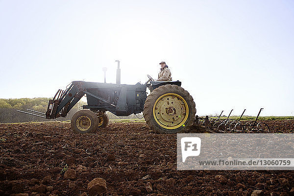 Landwirt fährt Traktor auf Feld gegen klaren Himmel