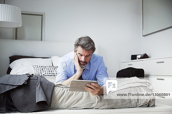 Businessman looking at tablet computer while lying on bed at hotel room