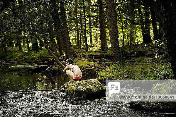 Rear view of girl sitting on rock in river