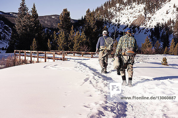 Rear view of fishermen walking on snowy field against mountain