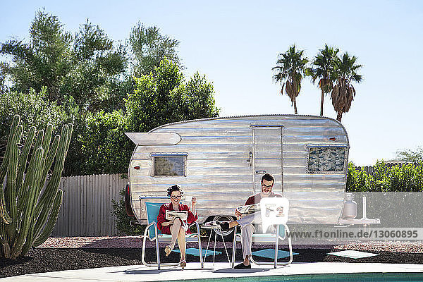 Ein Paar liest Zeitung  während es auf einem Stuhl gegen ein Wohnmobil sitzt