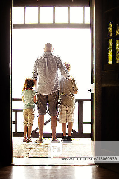 Rückansicht eines Vaters  der mit Kindern auf dem Balkon steht  durch eine Tür gesehen