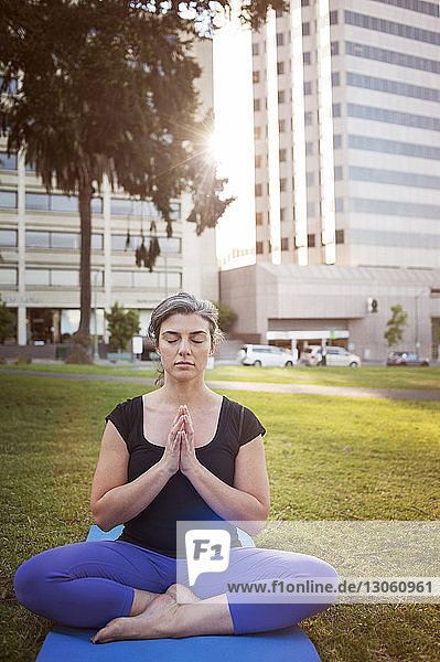 Frau meditiert  während sie auf einer Übungsmatte im Park sitzt