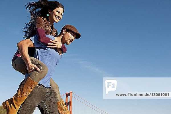 Low angle view of man piggybacking girlfriend against blue sky