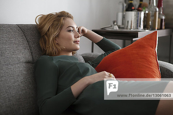 Woman looking away while lying on sofa at home