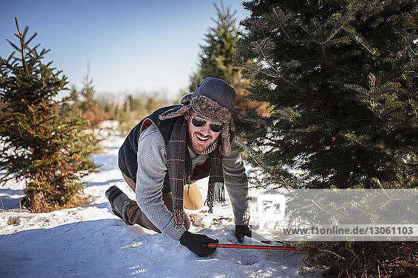Glücklicher Mann fällt Weihnachtsbaum auf schneebedecktem Feld