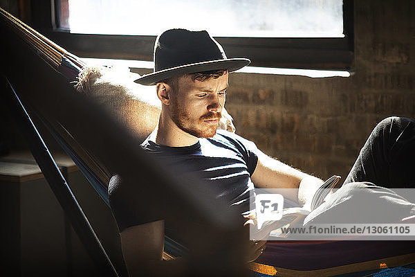 Mann mit Hut liest Buch  während er sich in der Hängematte entspannt