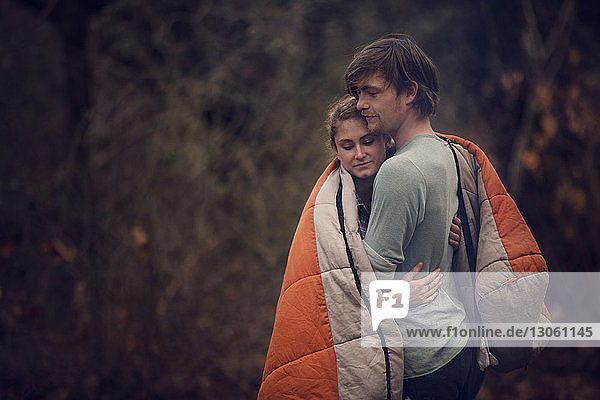 In eine Decke gehülltes Paar umarmt im Wald