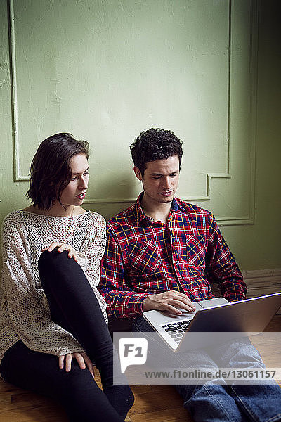 Ehepaar betrachtet Laptop  während es auf dem Boden sitzt