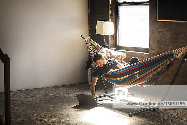 Man using laptop computer while lying in hammock tied on stand at home