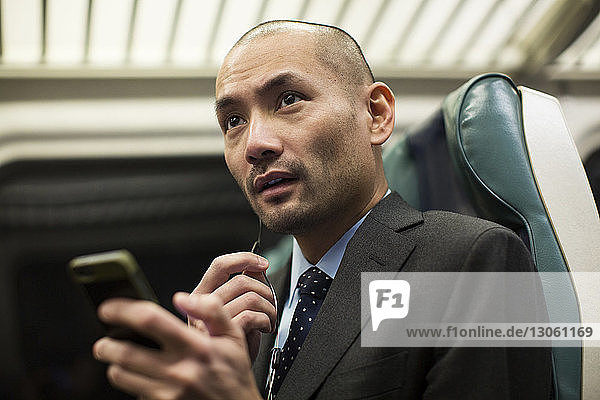 Geschäftsmann hält Smartphone während einer Zugfahrt in der Hand