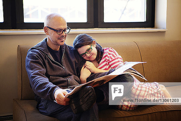 Vater und Tochter lesen Zeitung  während sie zu Hause auf dem Sofa sitzen