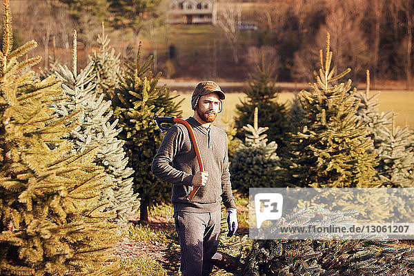 Man with hand saw looking away while standing in tree farm
