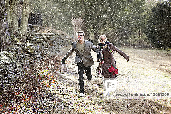 Happy couple running on field in forest during winter