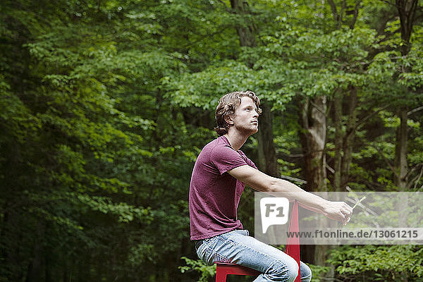 Seitenansicht eines Mannes  der auf einem Stuhl an Bäumen sitzt