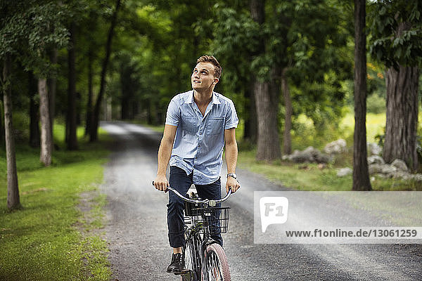 Happy man looking up while riding bicycle on road in woodland
