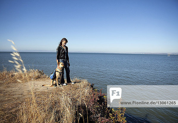Frau und Hund auf dem Feld gegen Meer und Himmel an einem sonnigen Tag