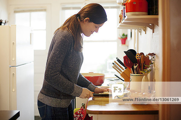 Seitenansicht einer Frau  die zu Hause in der Küche Gemüse auf einem Schneidebrett schneidet
