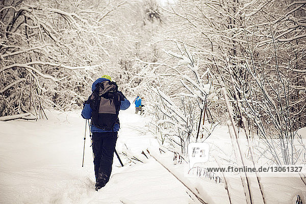 Rear view of male hiker carrying backpack while walking on snow covered field