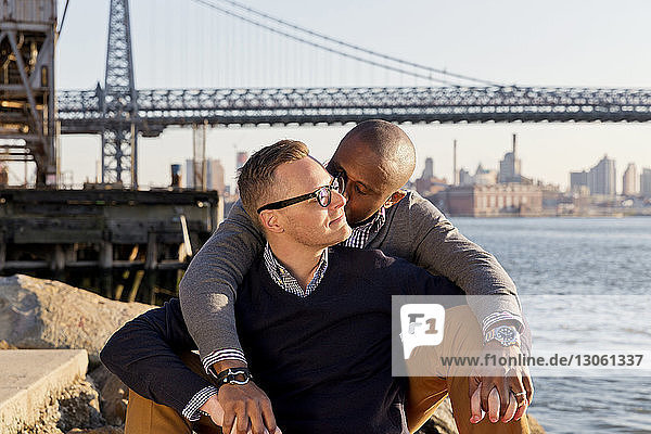 Man kissing boyfriend while sitting against Williamsburg Bridge