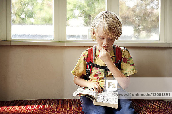 Boy reading book while sitting on sofa in library