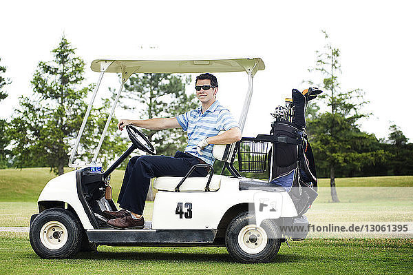 Porträt eines selbstbewussten Mannes  der im Golfwagen auf dem Feld sitzt