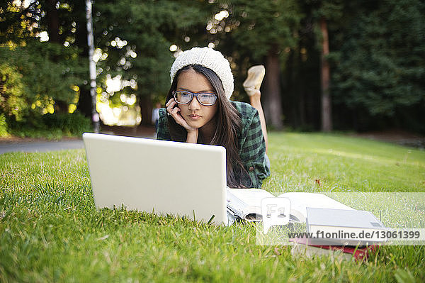 Frau benutzt Laptop  während sie im Park auf dem Rasen liegt
