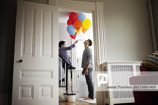 Woman holding helium balloons while standing on staircase by man at home