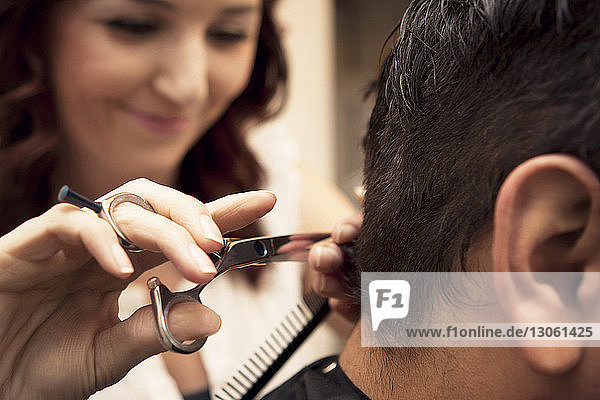 Nahaufnahme einer Friseurin  die die Haare eines männlichen Kunden im Salon schneidet