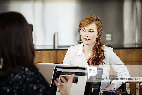 Businesswoman looking at colleague while having discussion in office