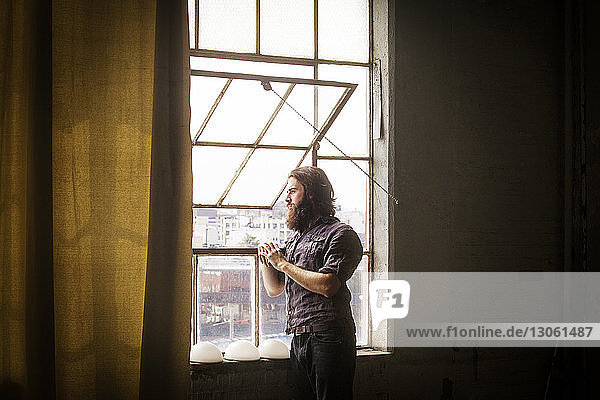 Thoughtful man standing by window at home