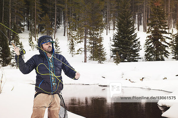 Fly fisherman casting fishing rod while standing on snowy field