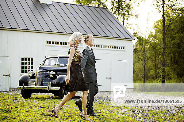 Senior couple walking on field against vintage car outside house