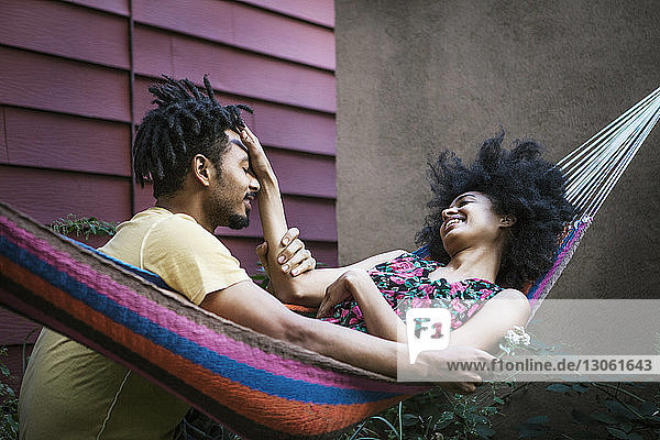 Woman playing with man's hair while lying on hammock in lawn