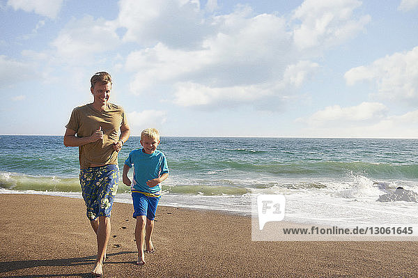 Father and son running at beach on sunny day