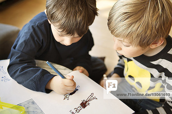 Hochwinkelansicht von Geschwistern  die zu Hause auf Papier zeichnen