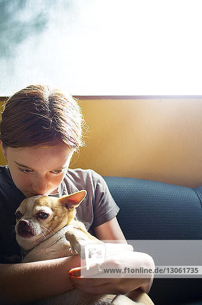 Mädchen umarmt Hund  während sie zu Hause auf dem Sofa sitzt