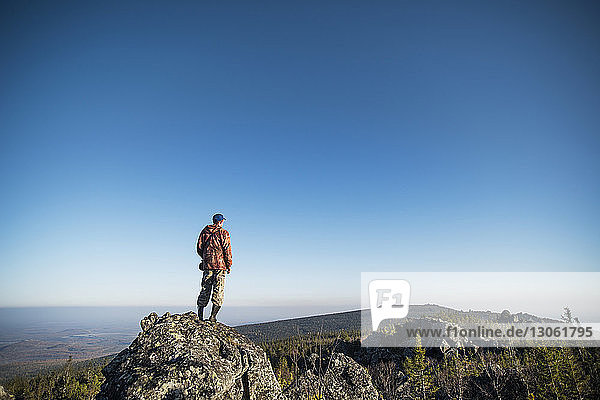 Rear view of hiker standing on mountain against clear sky
