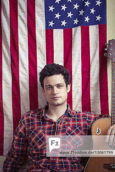 Porträt eines hübschen jungen Mannes mit Gitarre gegen amerikanische Flagge